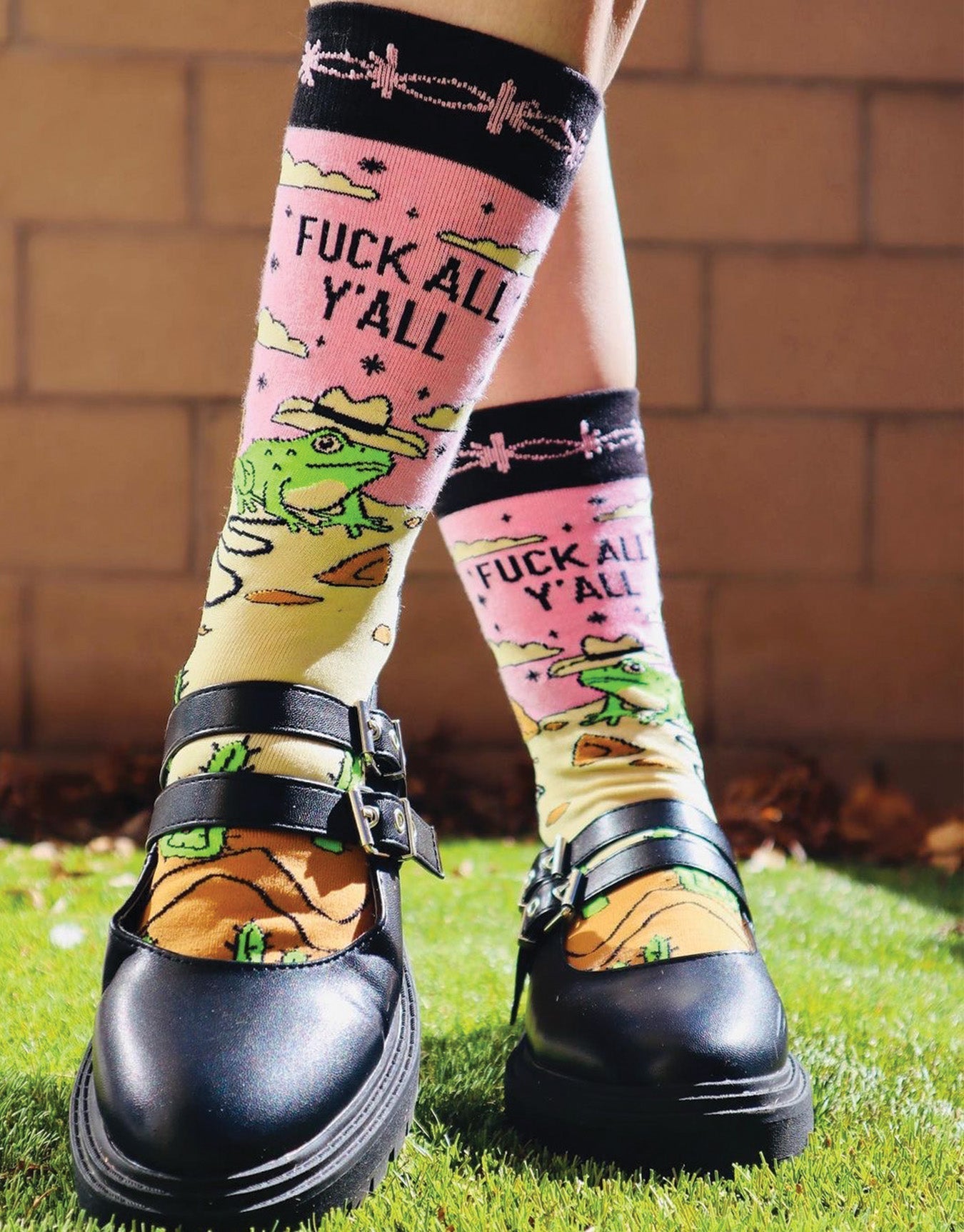 Model wearing a pair of socks with a frog and desert motif with the slogan F**k All Y'all on the ankle. Black toes, heel and cuff.