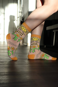 Make Today Your B**tch Socks. Model wearing a pair of socks depicting the sun and sunflowers with a bold sweary slogan. Orange toes, cuff and heel.