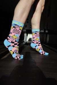 Model wearing a pair of socks with a bright pink and blue smiley face pattern and a bold sweary slogan. Blue toes, heel and cuff.