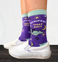 Model wearing a pair of socks with the slogan Manifest That S**t and a butterfly motif. Purple ankles, turquoise toe, heel and cuff.