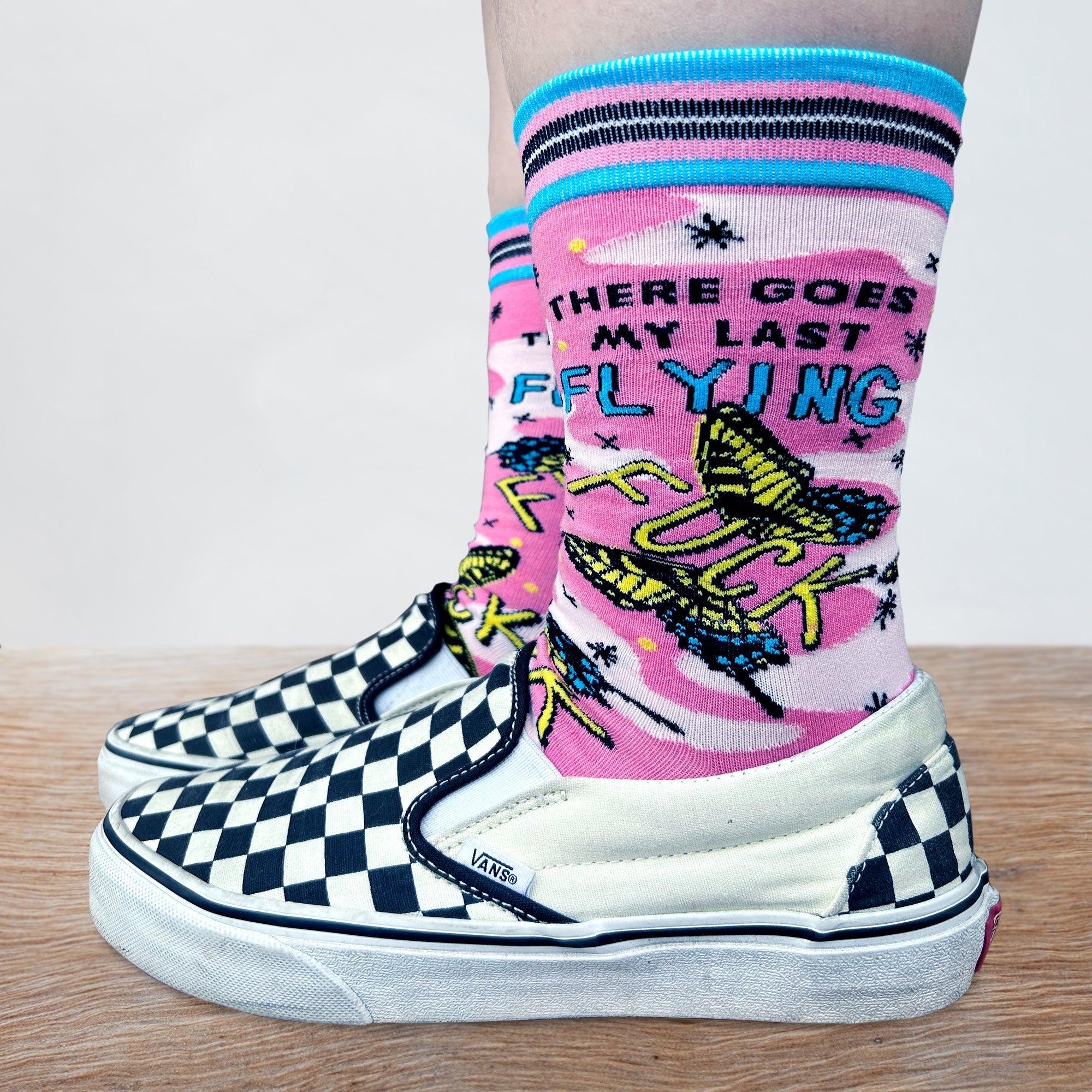 Last Flying F**k Socks - Small. Model wearing a pair of socks with a bold slogan and a pink and yellow butterfly motif. Bright blue heel, toe and cuff.